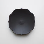A deep chocolate ceramic plate with a scalloped, flower-like rim, photographed from directly above on a clean white background.