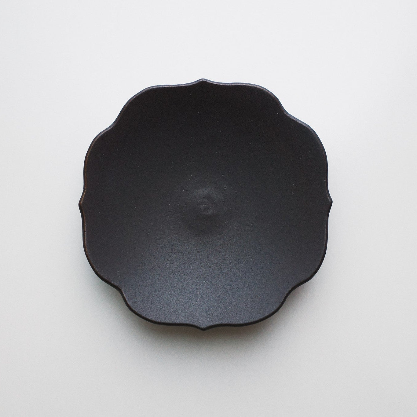 A deep chocolate ceramic plate with a scalloped, flower-like rim, photographed from directly above on a clean white background.