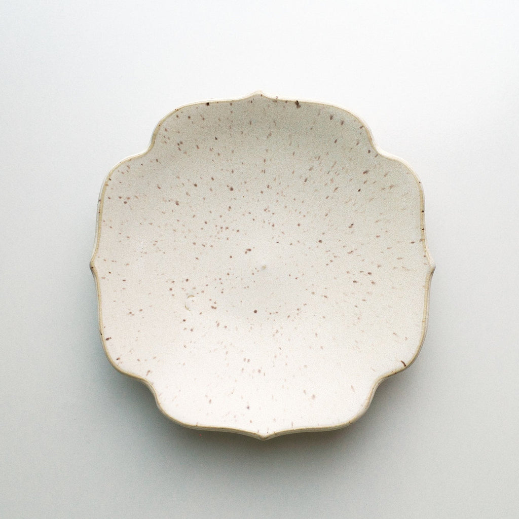 A small ceramic dish with a scalloped rim, featuring a speckled cream glaze and a natural unglazed edge, photographed from directly above on a light gray background.