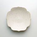A small ceramic dish with a scalloped rim, featuring a speckled cream glaze and a natural unglazed edge, photographed from directly above on a light gray background.