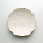 A small ceramic dish with a scalloped rim, featuring a speckled cream glaze and a natural unglazed edge, photographed from directly above on a light gray background.